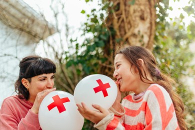 Zwei Personen blasen einen Luftballon aus mit dem Rotkreuz-Logo