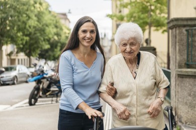 Eine Person begleitet eine ältere Frau bei einem Spaziergang