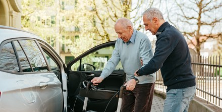 Eine Person hilft einem älteren Mann beim Einsteigen ins Auto