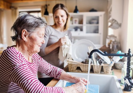 Eine Frau hilft einer älteren Frau beim Geschirr abwaschen